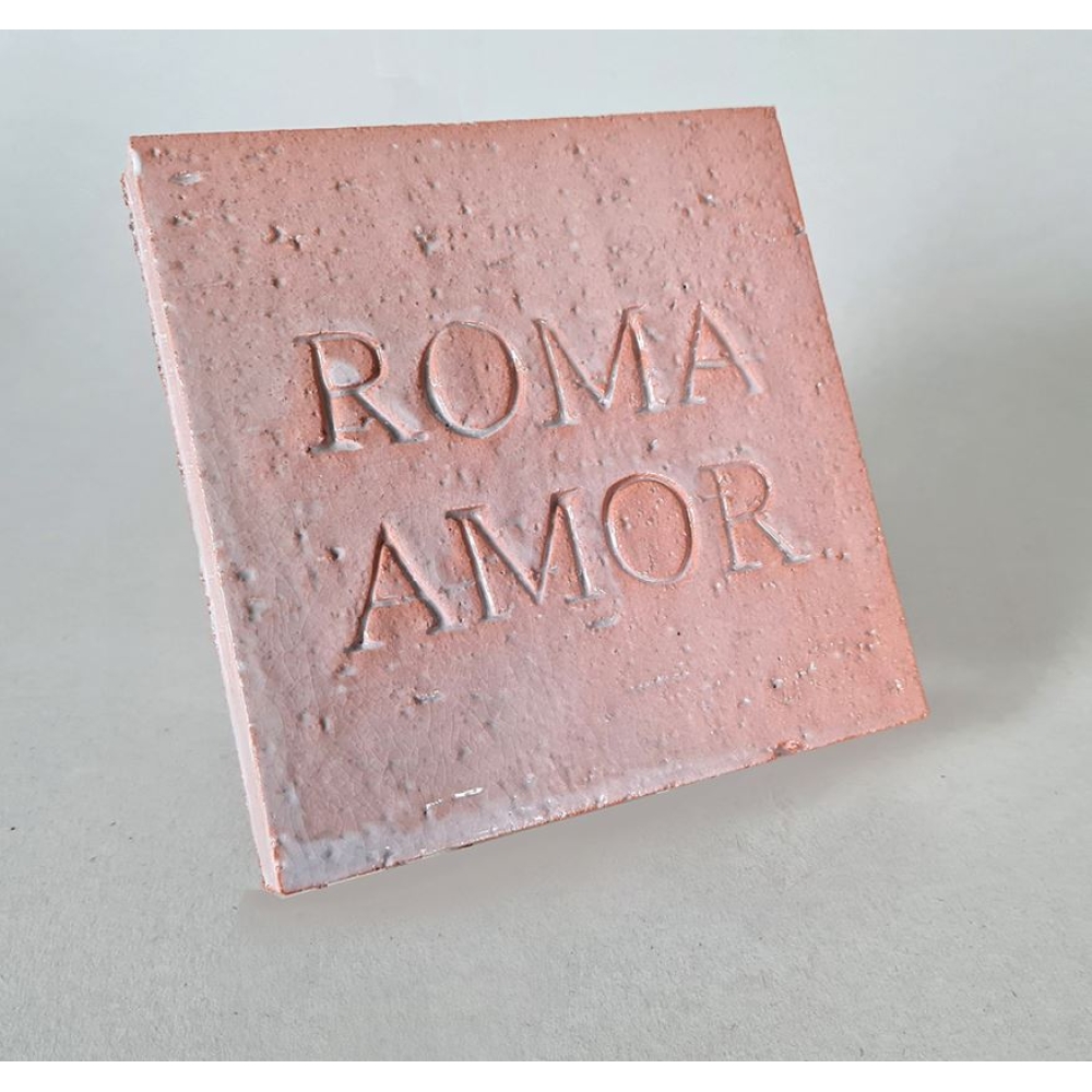 Pink ceramic tile souvenir with the embossed words “ROMA AMOR” on a neutral background