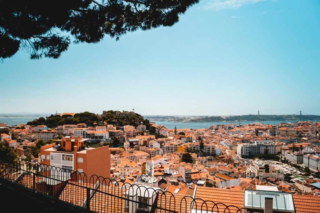 Panoramic view of Lisbon’s red-tiled rooftops and São Jorge Castle above the Tagus River on a sunny day