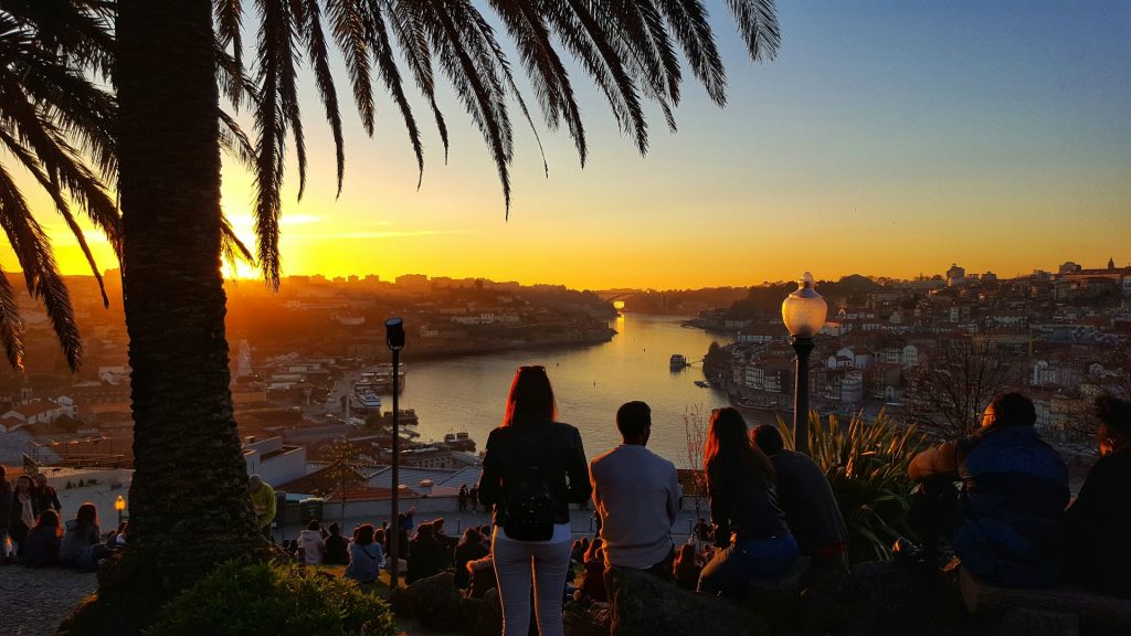 Sunset over Porto and the Douro River with people watching from the hillside viewpoint