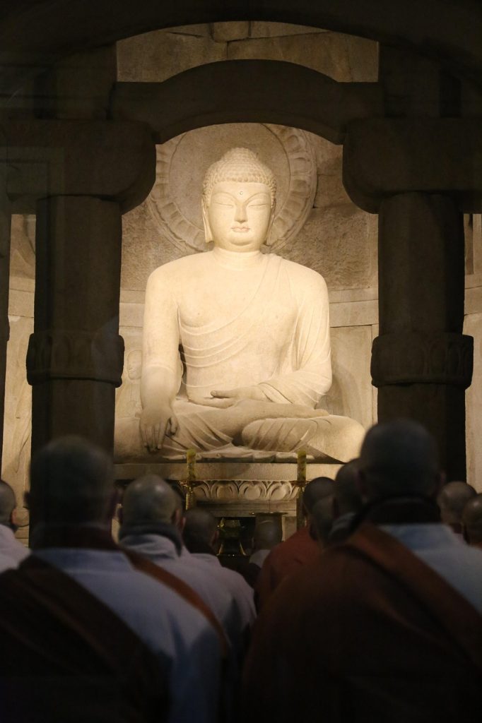 Stone Buddha statue inside a Seokguram Grotto Temple with worshippers.